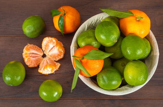 top view mandarins in basket and green lemons on wood surface