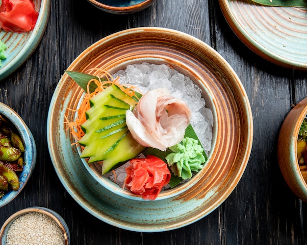 Top view of marinated herring fillets with sliced cucumbers ginger and wasabi sauce on ice cubes in a plate on the wood table