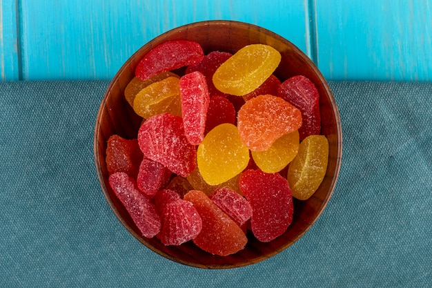 Top view of marmalade candies in a wooden bowl on blue