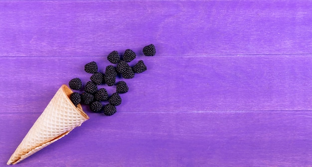 Top view marmalade in the form of a blackberry with a waffle cone on a purple background