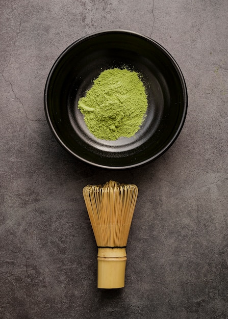 Top view of matcha tea powder in bowl with bamboo whisk