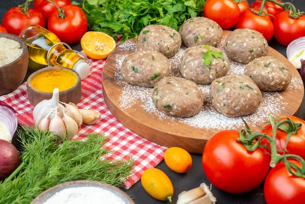 Top view of meat balls on a brown board and rice flour fresh green lemon fallen oil bottle fresh vegetables yellow ginger on red stripped towel on black background