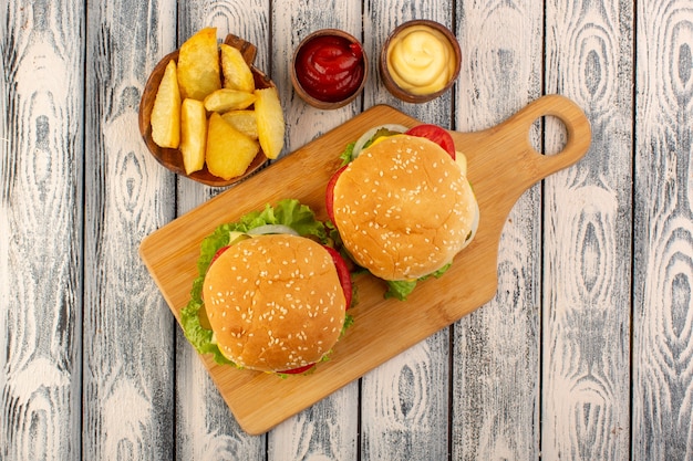 A top view meat burger with cheese and green salad potatoes and dips