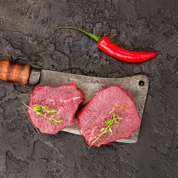 Top view of meat on cleaver with herbs and chili