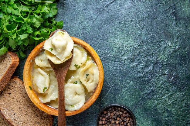 Top view meat dumplings inside wooden plate with greens and bread loaves on dark blue surface