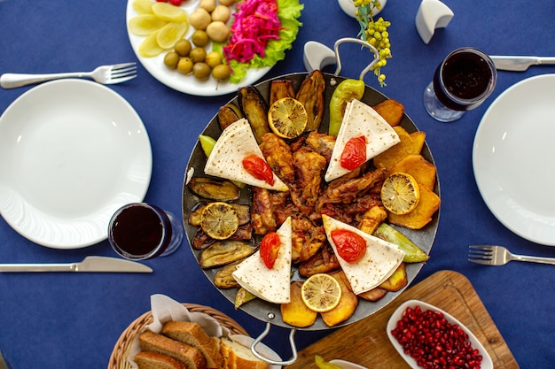 A top view meat meal cooked along with pomegranate and fresh vegetables with bread slices on the blue table