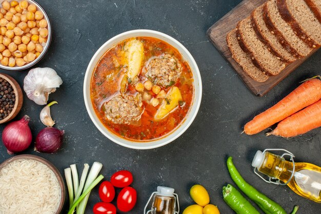 Top view meat soup with bread loafs and seasonings on dark background