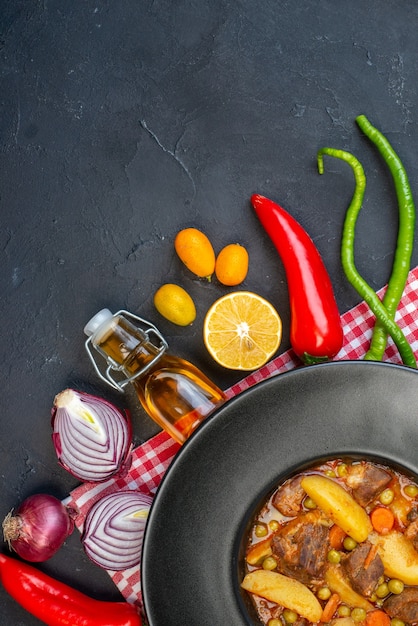 Top view meat soup with garniture on round plate fresh vegetables on black table with copy place