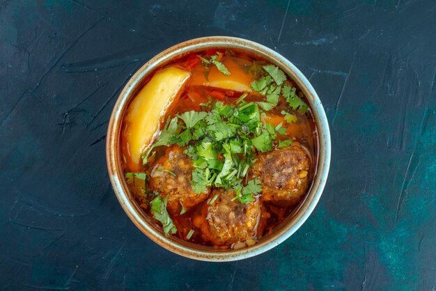 Top view meat soup with meatballs greens and sliced potatoes on dark-blue desk