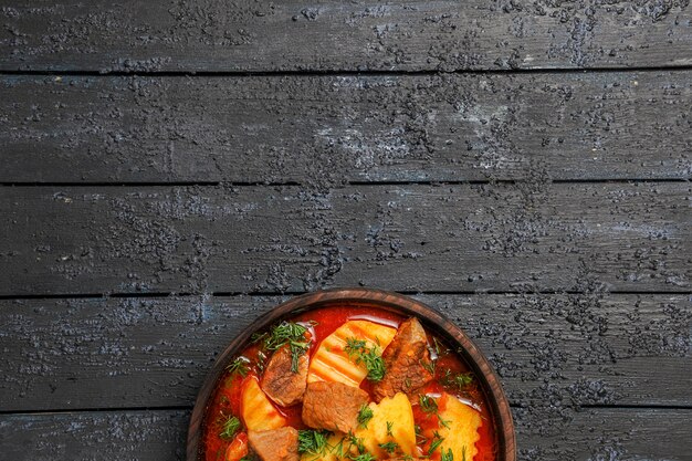 Top view meat soup with potatoes and greens on dark background