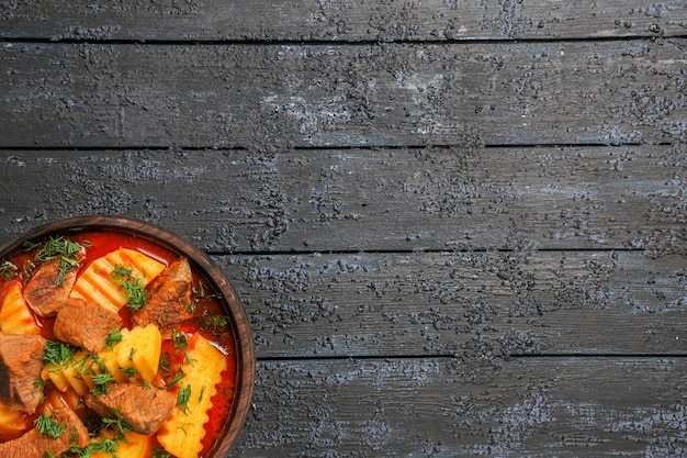 Top view meat soup with potatoes and greens on a dark desk