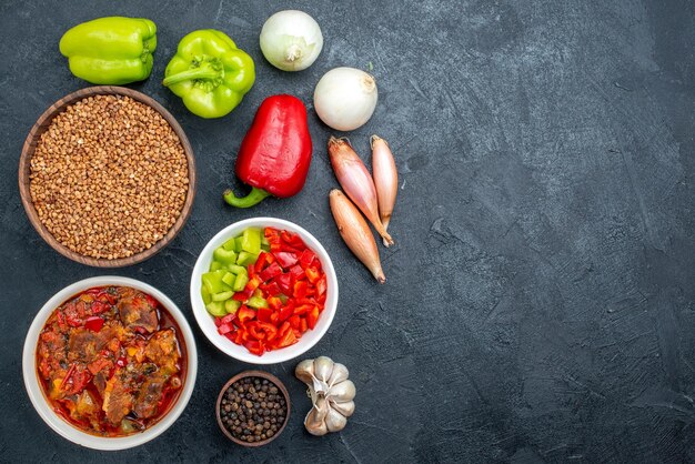 Top view meat soup with vegetables and raw buckwheat on dark space