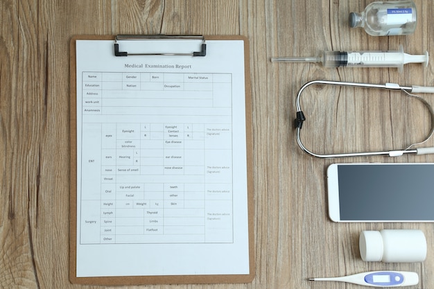 Top view of medical examination report,cellphone,and medical equipments on wooden desk