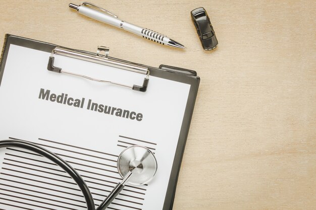Top view medical insurance form with stethoscope,car on wooden background.