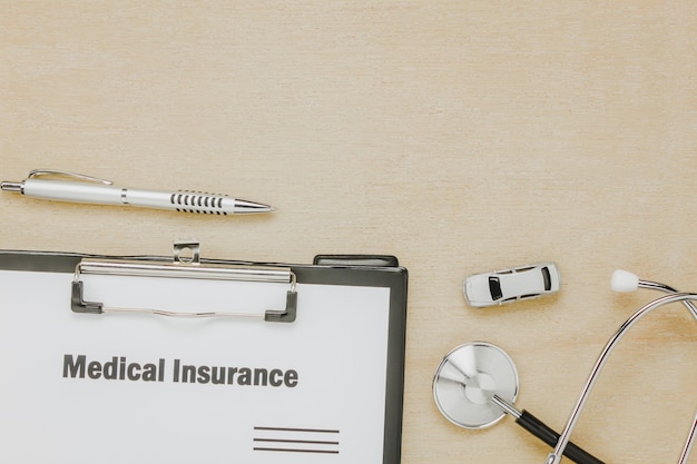 Top view medical insurance form with stethoscope,car on wooden background.