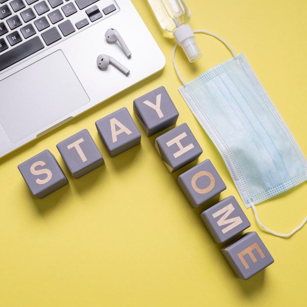 Free photo top view of medical mask with wooden cubes saying stay home next to laptop