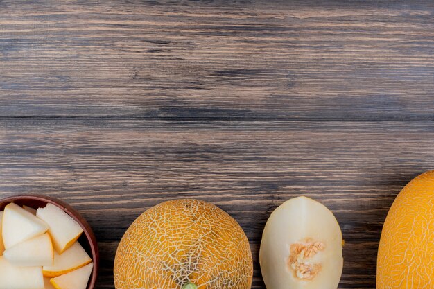 Top view of melon slices in bowl with cut and whole ones on wooden background with copy space