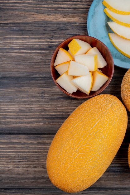 Top view of melon slices in bowl with whole and sliced ones on wooden background