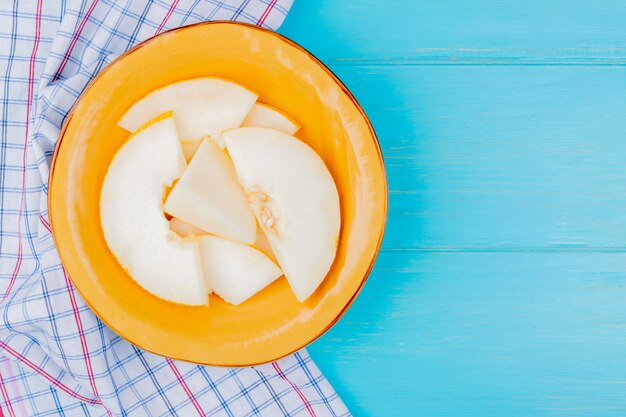 Top view of melon slices in plate on plaid cloth and blue background with copy space