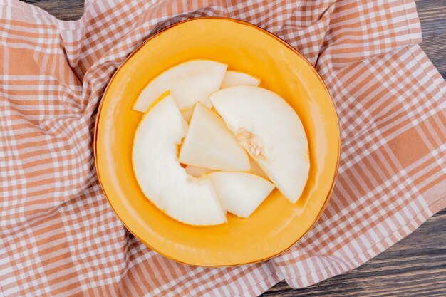 Top view of melon slices in plate on plaid cloth and wooden background