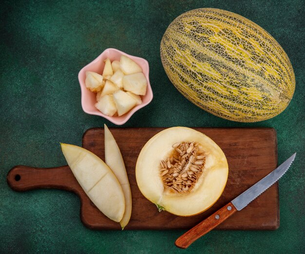 Vista dall'alto di fette di melone su una tavola di cucina in legno con bucce con coltello sulla superficie verde