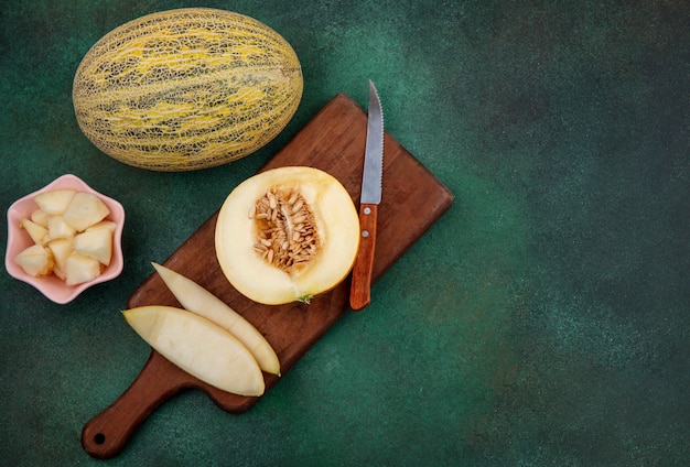 Top view of melon on a wooden kitchen board with knife with peels on green surface
