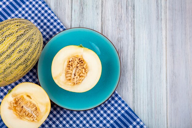 Top view of melons on a blue plate on blue checked tablecloth on grey wooden surface