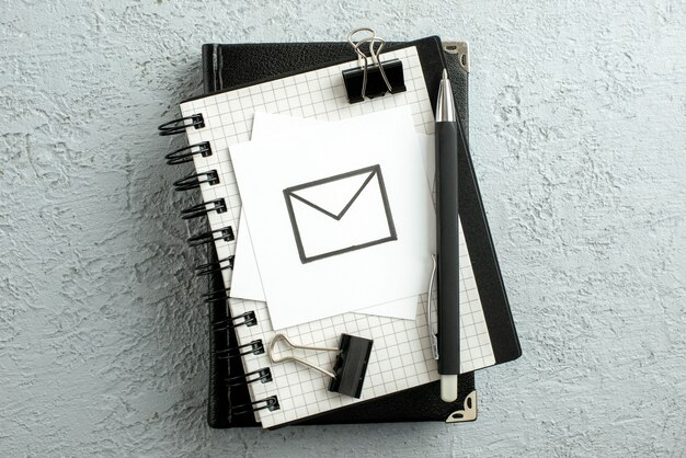 Top view of message drawing on white sheet pen on spiral notebook and book on gray sand background