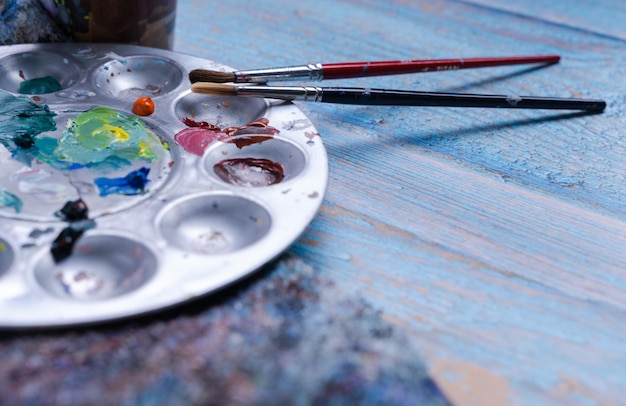 Top view of a metal painting pallet with brushes on a cloth and weathered blue wooden surface