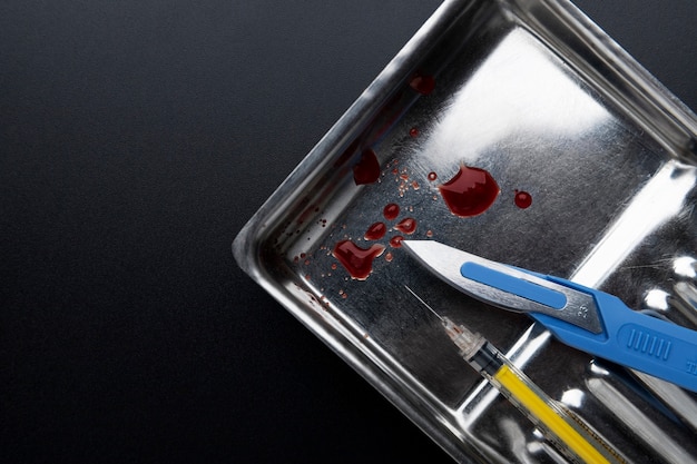 Top view of metallic medical scalpel with blood and syringe