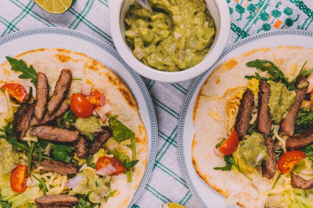 Top view of mexican beef stripes in tortilla with bowl of guacamole over table cloth