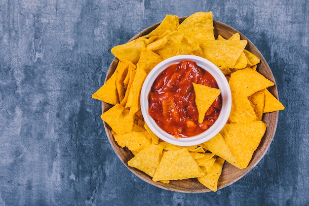 Top view of mexican nachos chips with spicy salsa sauce in container