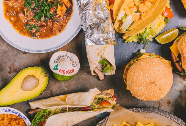 Top view of mexican tacos; beef dish; avocado and burger over old metal background