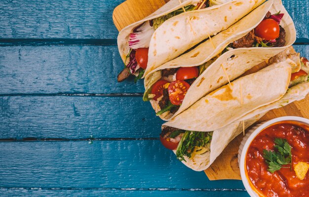 Top view of mexican tacos; salsa sauce with meat and vegetables on cutting board