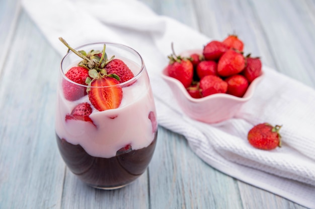 Top view of milkshake with chocolate and strawberries on a glass with strawberries on a bowl on grey surface
