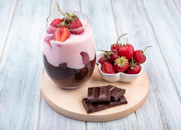 Top view of milkshake with strawberries and chocolate on a wooden kitchen board on grey surface
