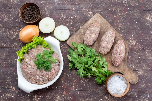 Top view minced raw meat inside plate with greens onions salt on the brown desk meat raw food meal green