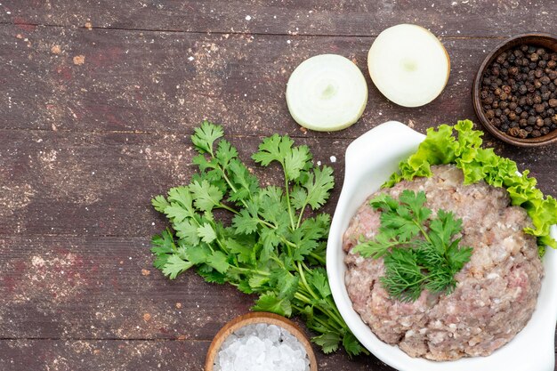 Top view minced raw meat with greens inside plate with onions salt on the brown desk meat raw food meal green photo