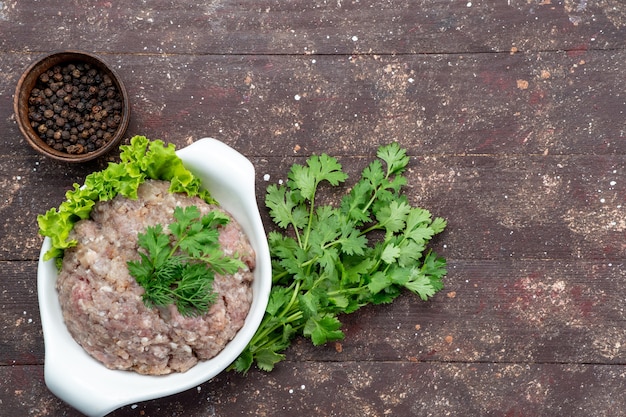 Free photo top view minced raw meat with greens inside plate with seasonings on the brown background meat raw food meal green photo