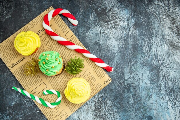 Top view mini cupcakes xmas ornaments on newspaper on dark surface