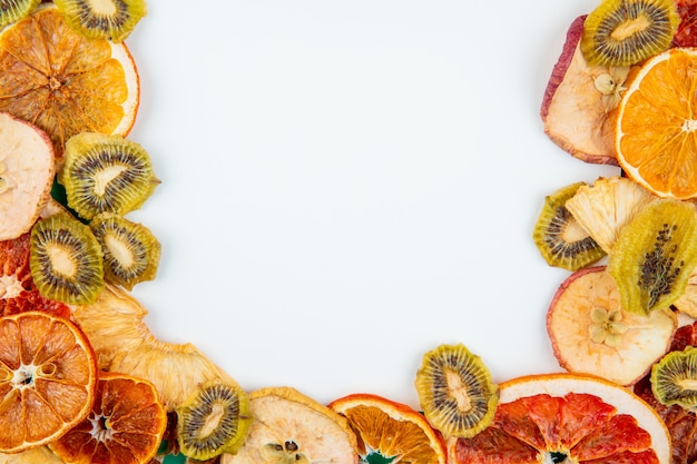 Top view of mix of dried fruits and citruses apple orange kiwi and pineapple slices on white background with copy space