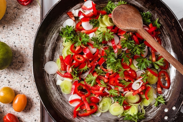 Top view of the mix of fresh vegetables in the rustic pan with a wooden spoon