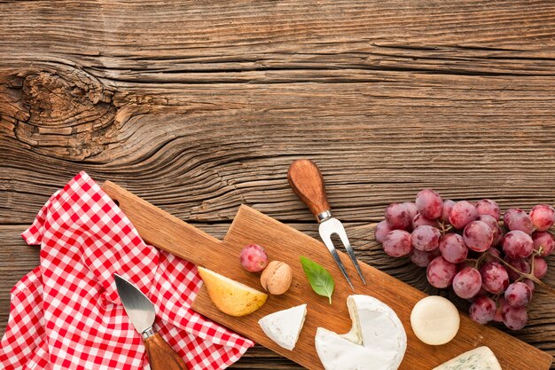 Top view mix of gourmet cheese on wooden cutting board with grapes