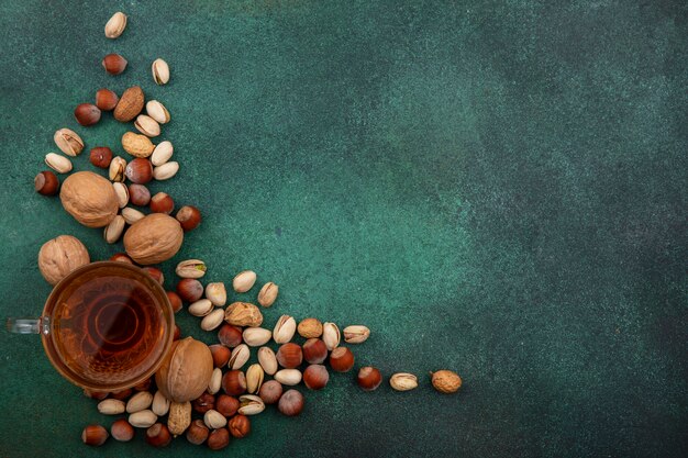 Top view of mix of nuts, walnuts, pistachios, hazelnuts and peanuts with a cup of tea on a green surface