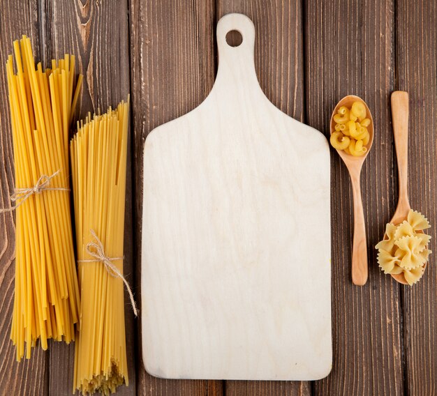 Top view mix pasta elbow macaroni farfalle bucatini and spaghetti pasta on wooden background