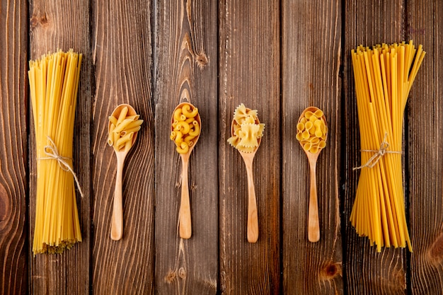 Top view mix pasta spaghetti bucatini farfalle penne elbow macaroni and farfalle tonde on wooden background