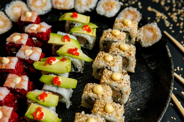 Top view mix rolls with avocado sesame seeds and chopsticks on a stand