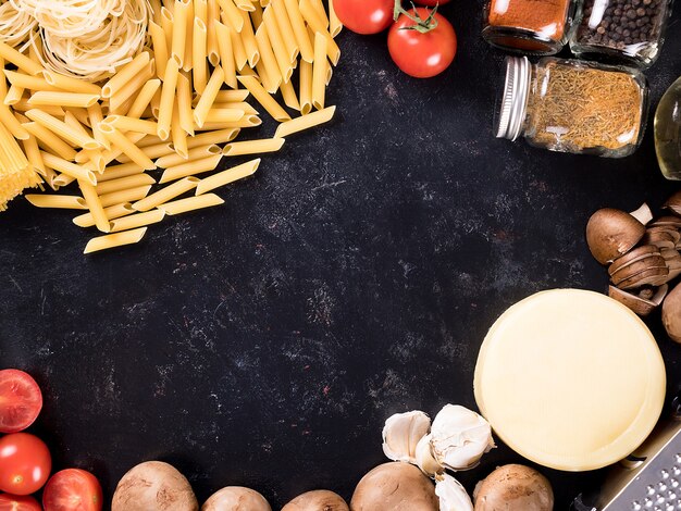 Top view mix of uncooked raw pasta, spaghetti, macaroni next to mushrooms, cheese, tomato souce, fresh tomateos, spices and sunflower oil. Copyspace available