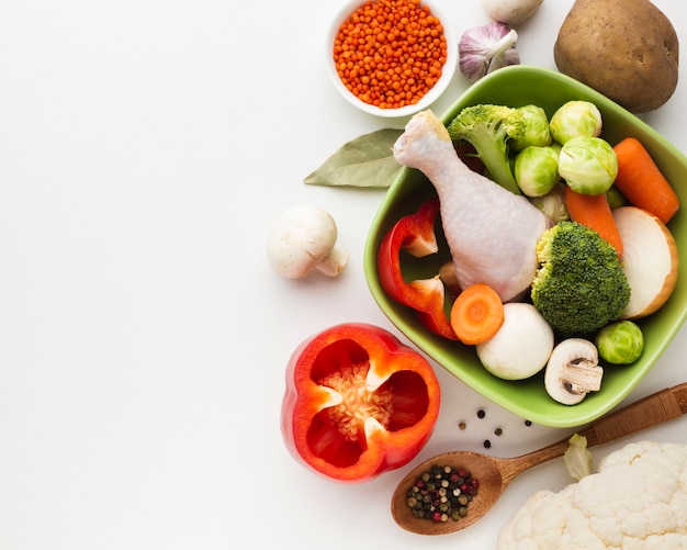 Top view mix of vegetables in bowl and chicken drumstick with copy space