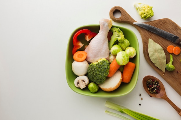 Top view mix of vegetables on cutting board and in bowl with chicken drumstick and spoon with copy space